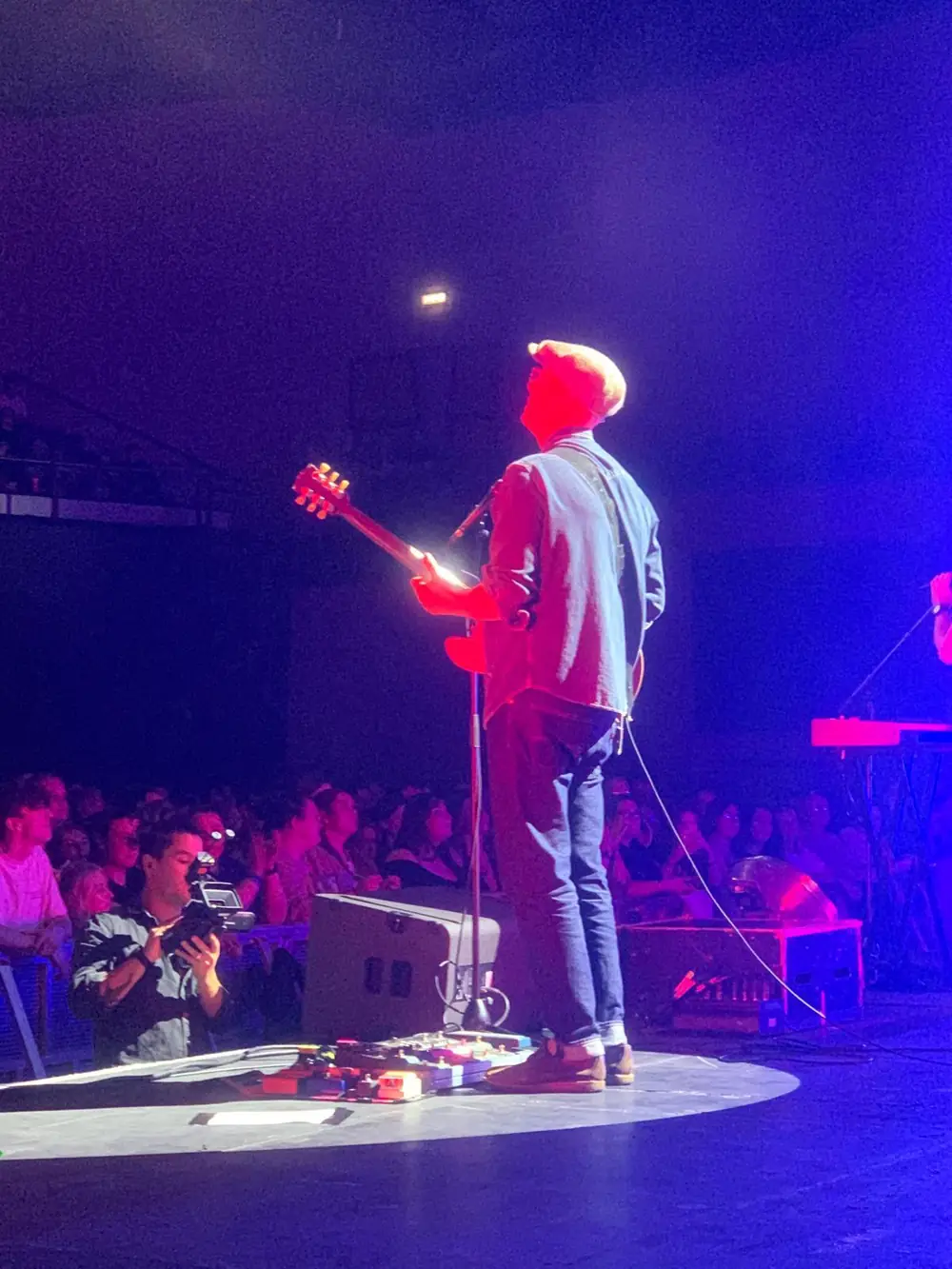 Connor McDonald playing guitar alone on a circular stage under red and purple light