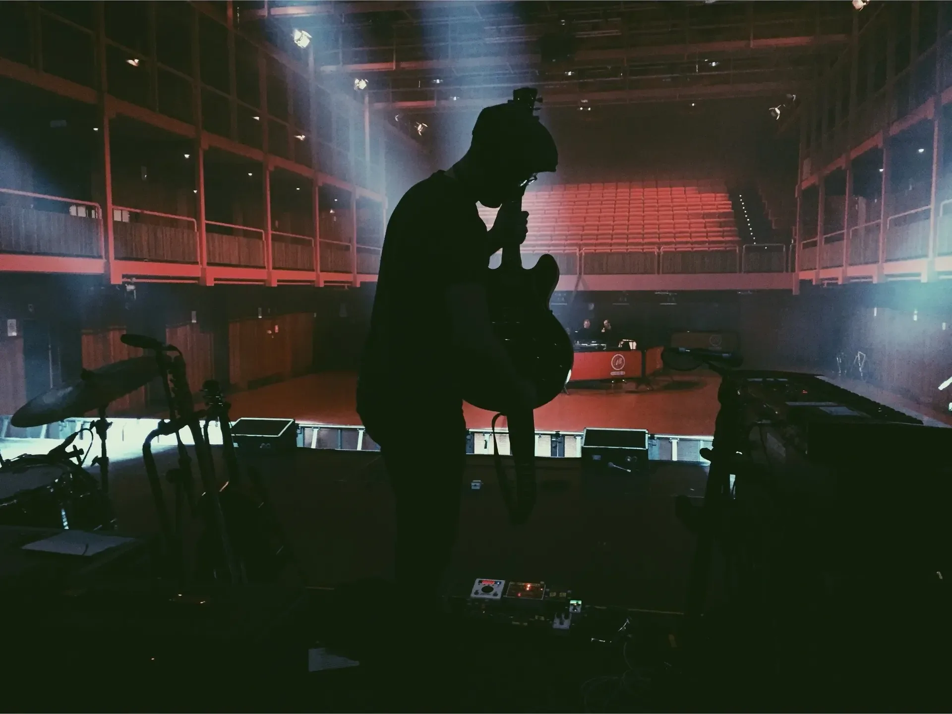 Connor McDonald silhouetted with a guitar on stage in an empty concert hall during soundcheck