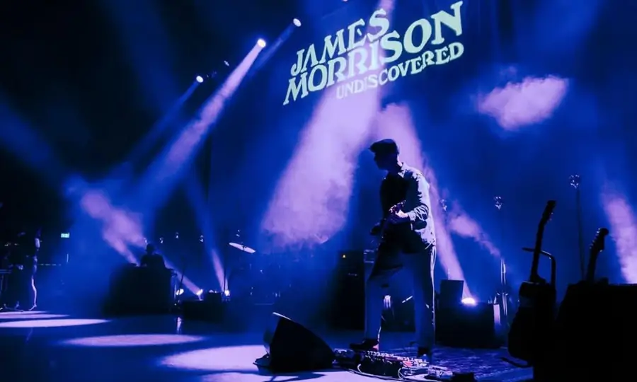 Connor McDonald silhouetted in blue stage light beneath a James Morrison backdrop