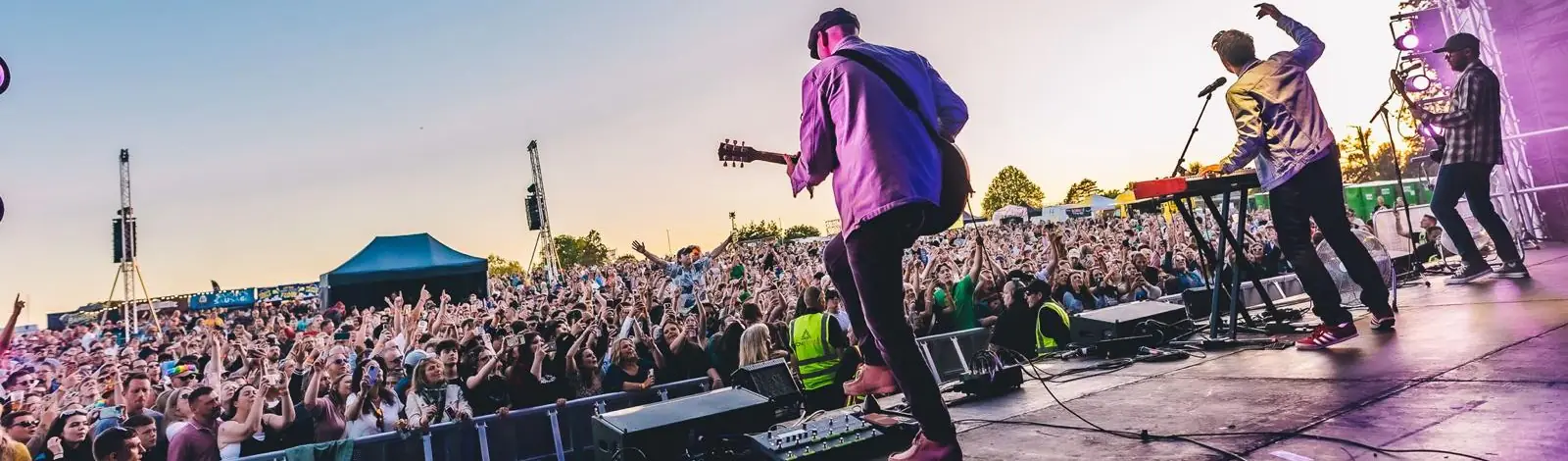 Festival main stage at sunset with the crowd's hands in the air