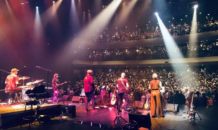 Connor McDonald on stage with the band at a packed theatre under warm light