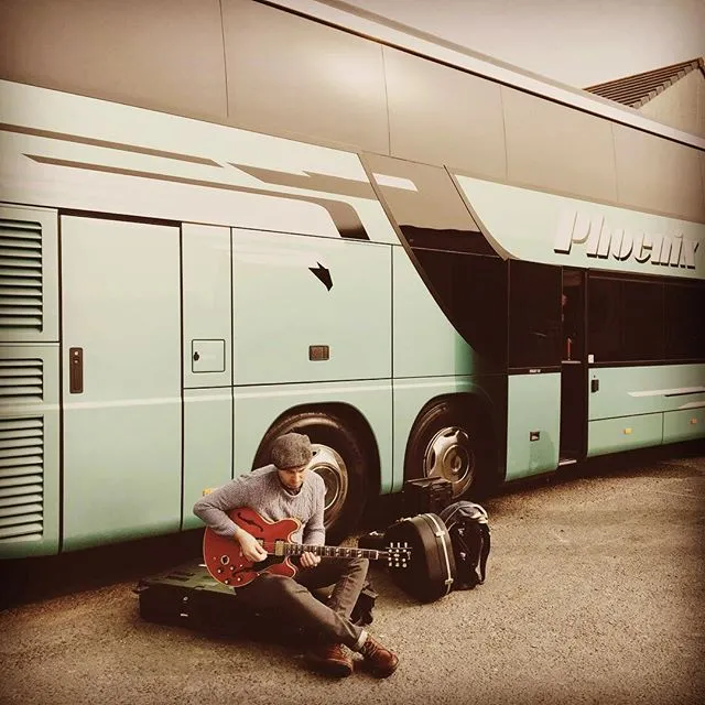 Connor sitting beside the tour bus with a guitar case
