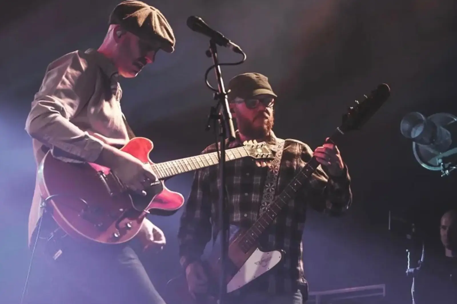 Connor McDonald playing electric guitar on stage alongside a bandmate under pink stage light